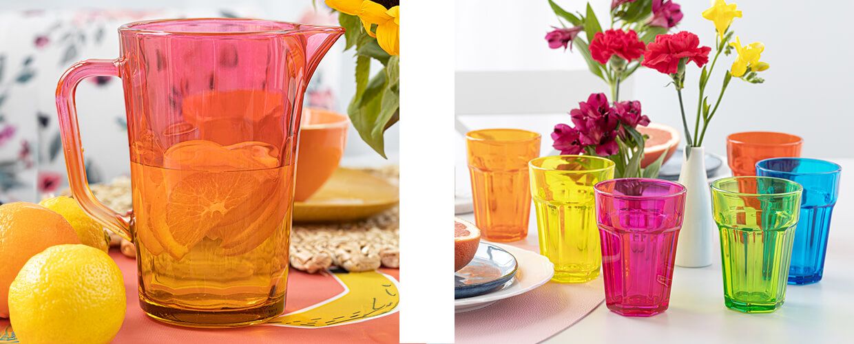 Kolorowy, pomarańczowy dzban pełen napoju z plasterkami pomarańczy, obok zestaw kolorowych szklanek Gigi Colorful Boom